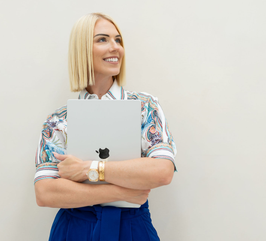 Jessica Gwynne holding a laptop and smiling in a cream-toned room.